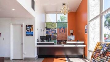 A reception desk with a computer, a chandelier, and a window with a view of trees.