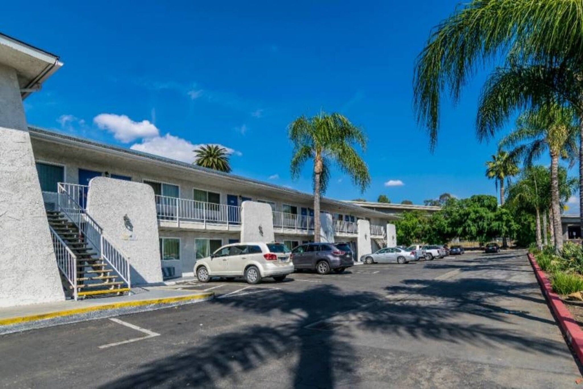 Un motel con estacionamiento, una escalera que lleva a la entrada y palmeras.
