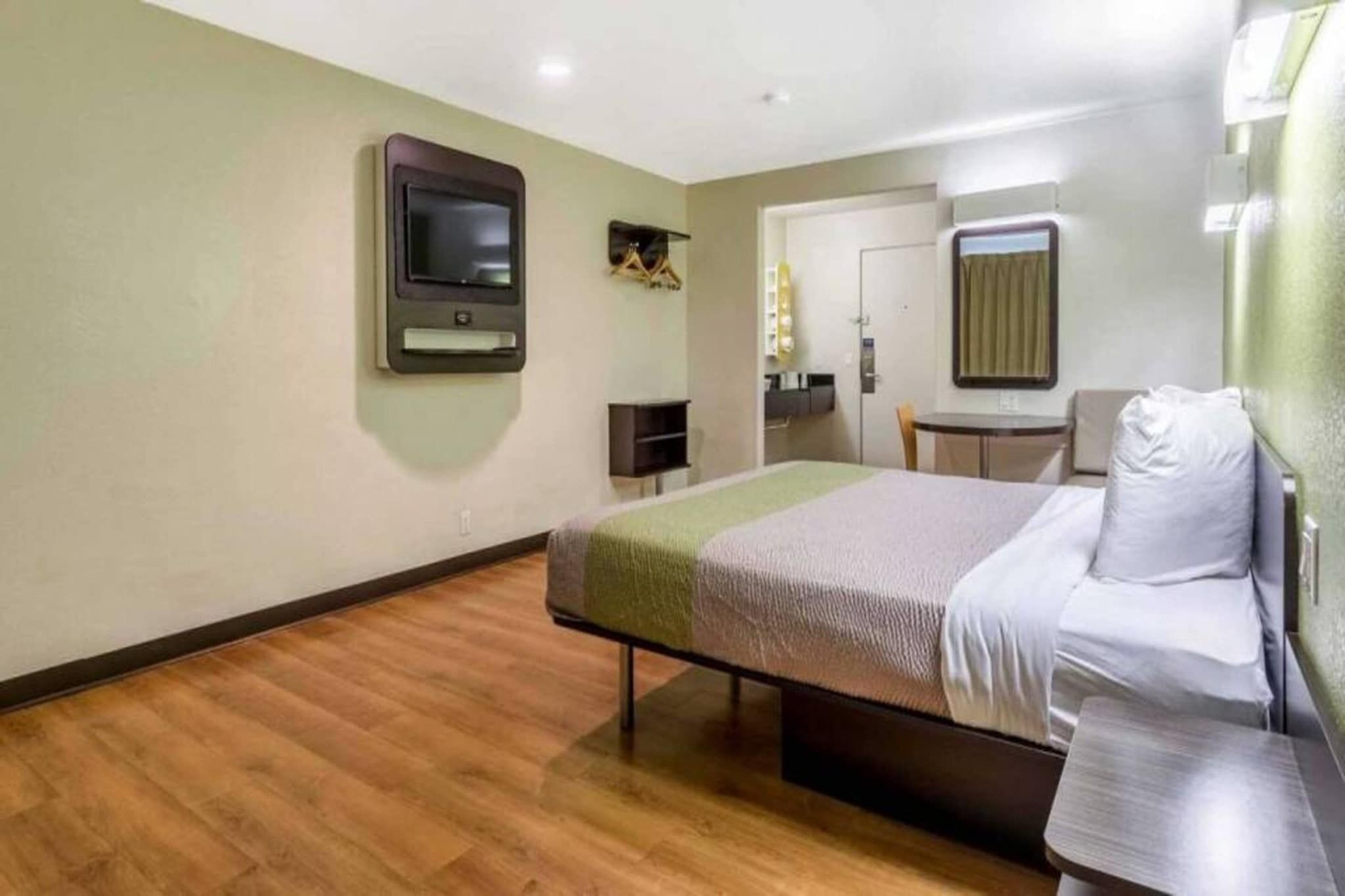 A hotel room with a bed, a desk, a chair, a television mounted on the wall, and a mirror.