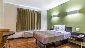 A hotel room with a bed, a desk, a chair, a window with curtains, and a wall-mounted air conditioner. - 1 KING BED | MOBILITY ACCESSIBLE NON-SMOKING (REDLANDS)