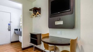 A hotel room with a dining table, chairs, a TV mounted on the wall, a small shelf, and a door. - 1 KING BED | MOBILITY ACCESSIBLE NON-SMOKING (REDLANDS)