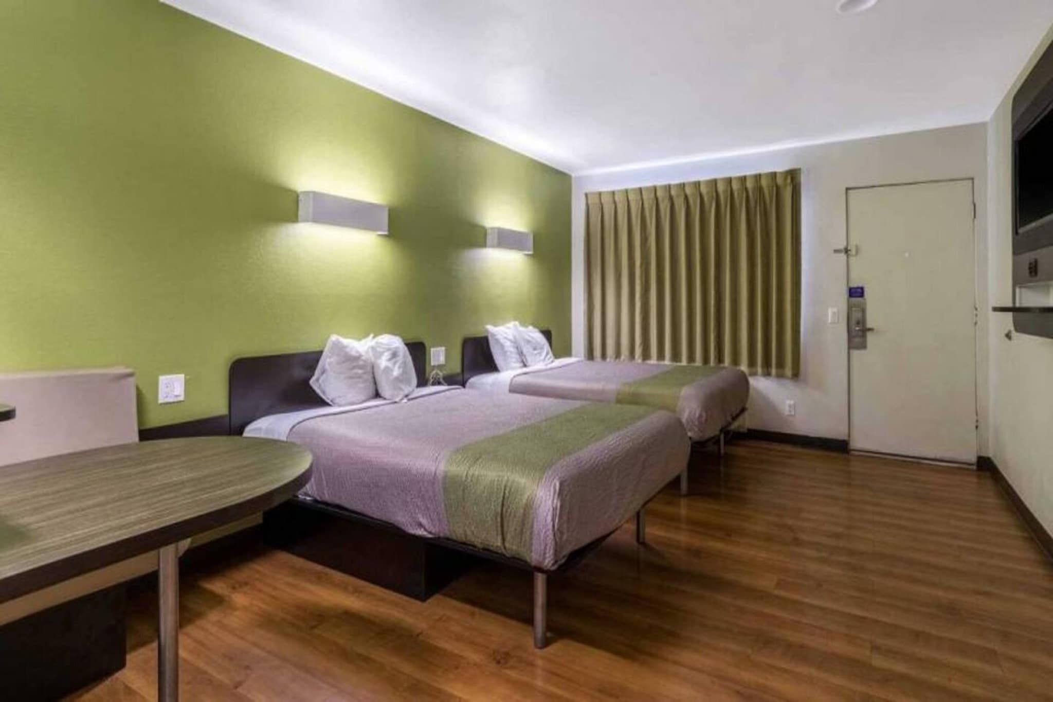 A hotel room with two beds, a wooden floor, a small table, and a door.