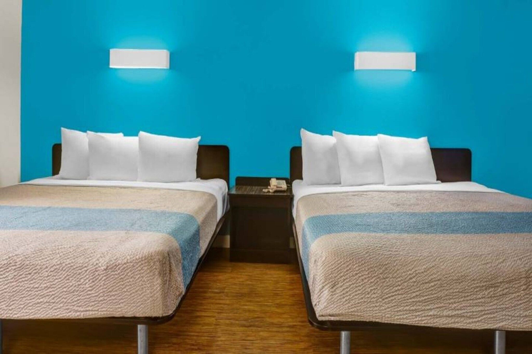 A hotel room with two beds, a wooden floor, and a blue wall.