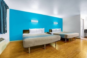 Quarto de hotel com duas camas, parede de destaque azul e piso de madeira.