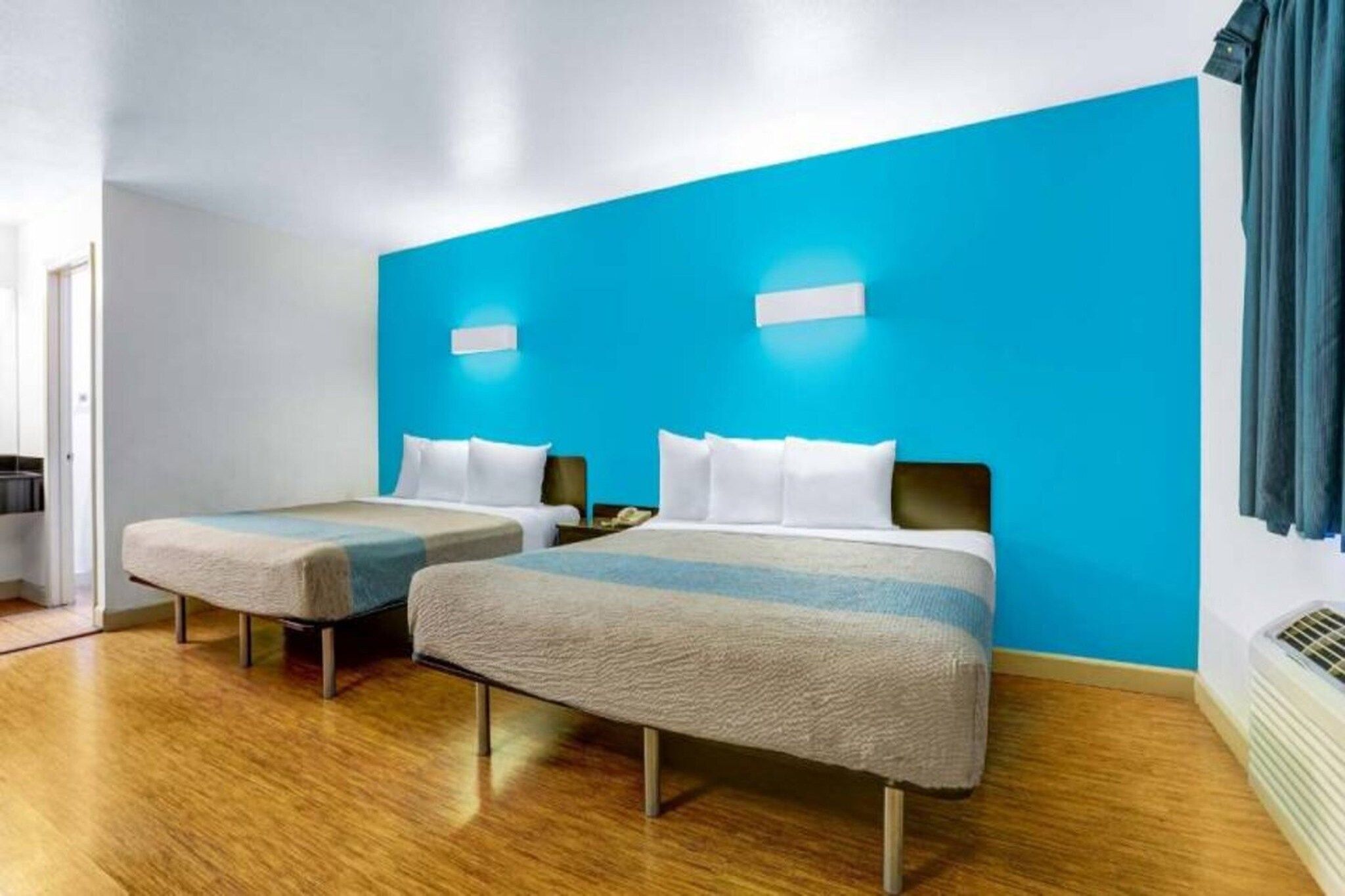 A hotel room with two beds, a blue accent wall, and a wooden floor.
