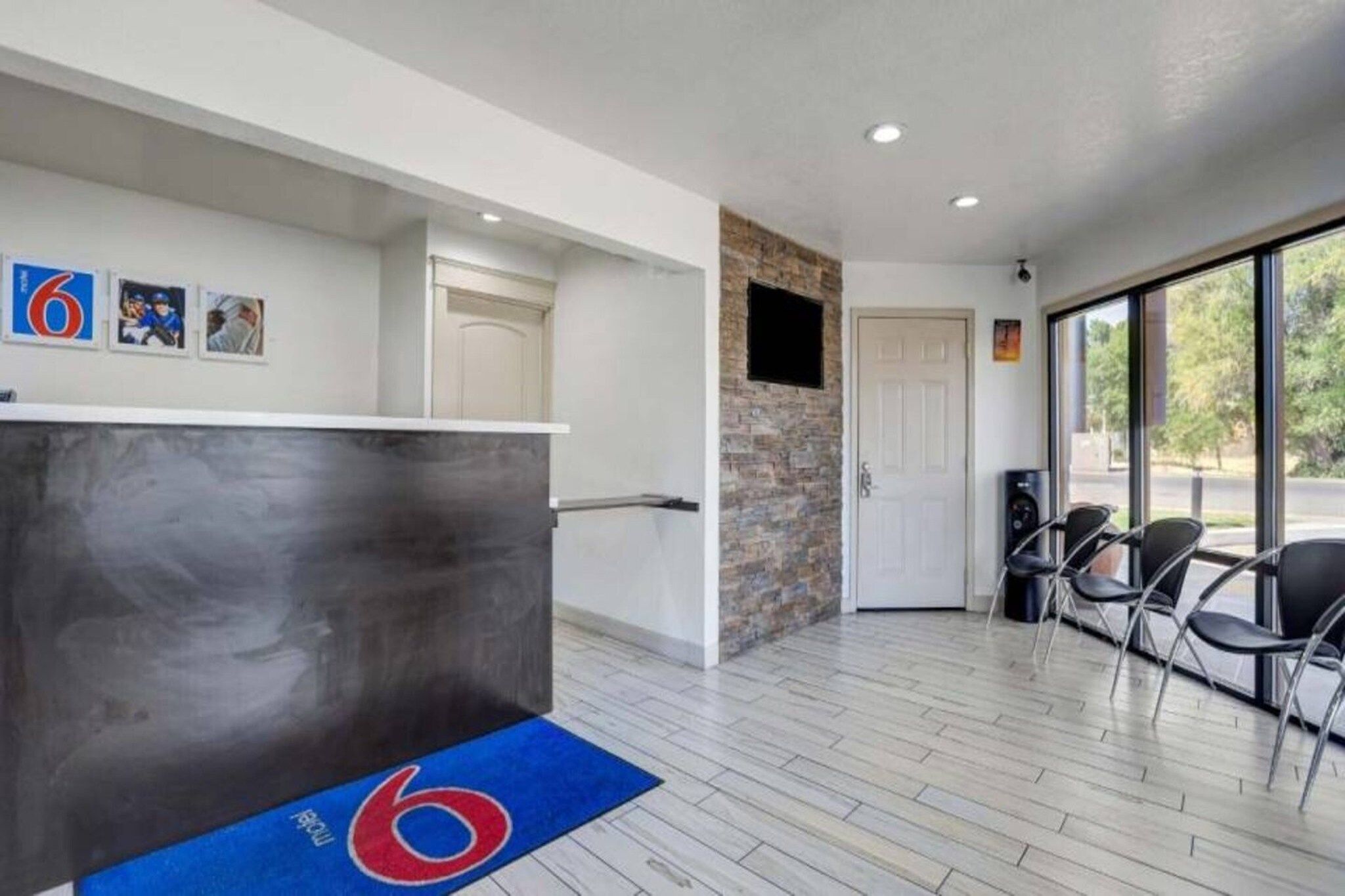 A reception area with a reception desk, a blue carpet with a logo, a stone wall, and a door leading to a balcony with chairs.