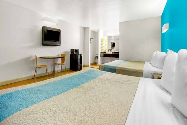 A hotel room with a bed, a desk with a chair, a television, and a kitchenette.