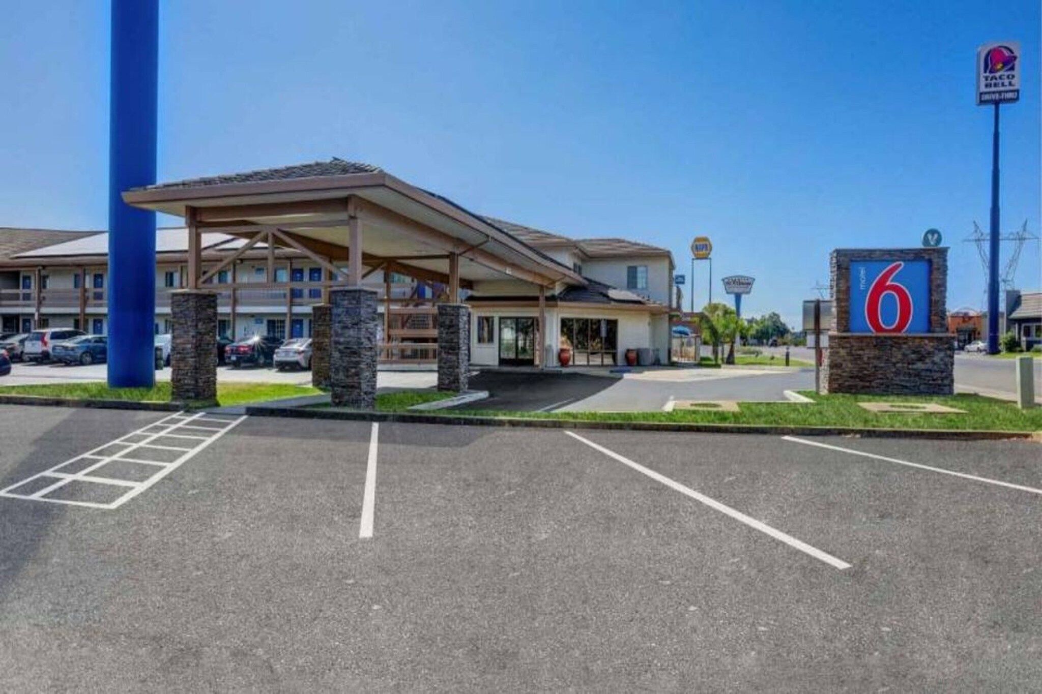 Een motel met een overdekte parkeerplaats, een bord met het nummer 6 en een Taco Bell drive-thru.
