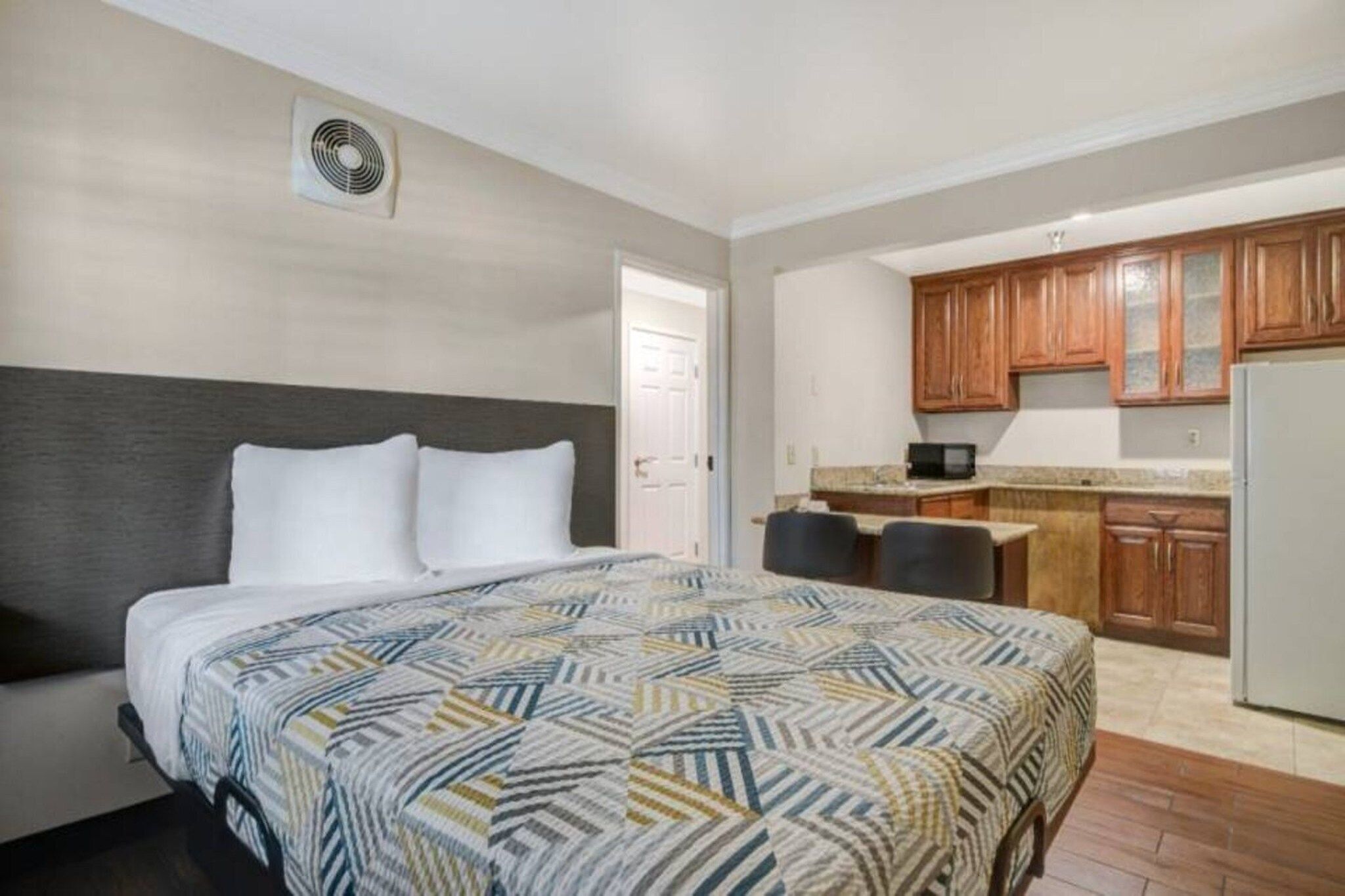 Quarto de hotel com cama, cozinha compacta e porta que dá para outro quarto.