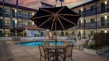 A hotel pool area with multiple umbrellas, lounge chairs, and a pool.