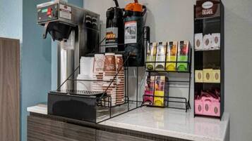 Uma estação de café com máquina de café, moedor e diversos sachês de café.