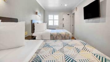 A hotel room with two beds, a television mounted on the wall, and a window providing natural light.