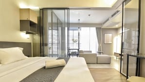 Una habitación de hotel moderna con cama, sofá, una mesita y un separador de vidrio.