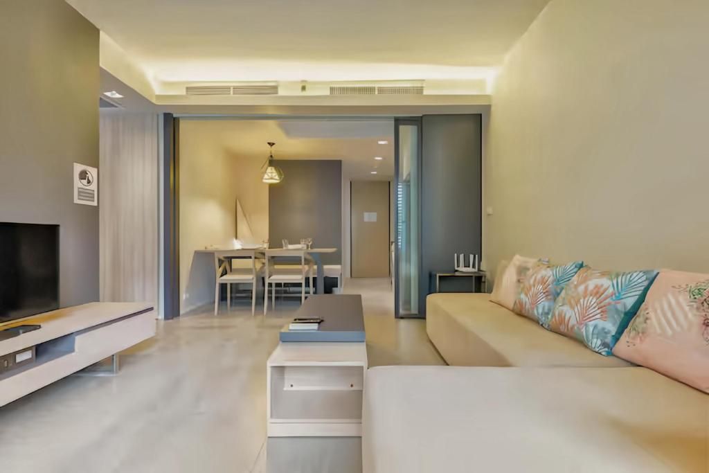 A modern living room with a sofa, a flat-screen TV, and a dining area with a table and chairs.