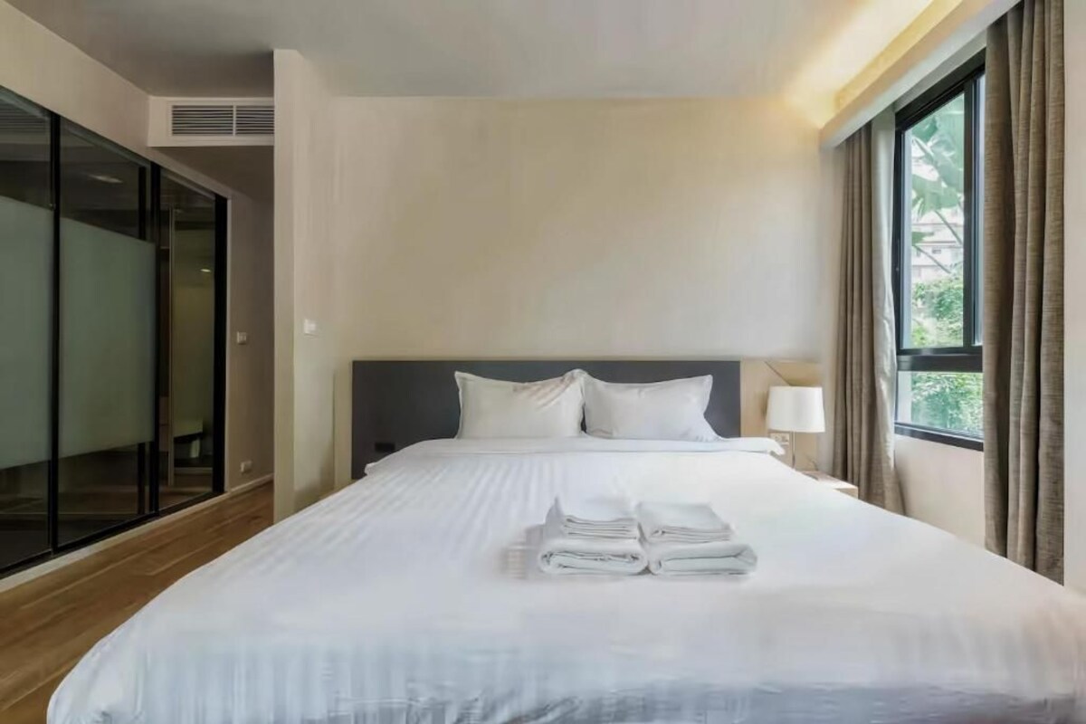 A hotel room with a bed, a nightstand, a lamp, and a window with curtains.
