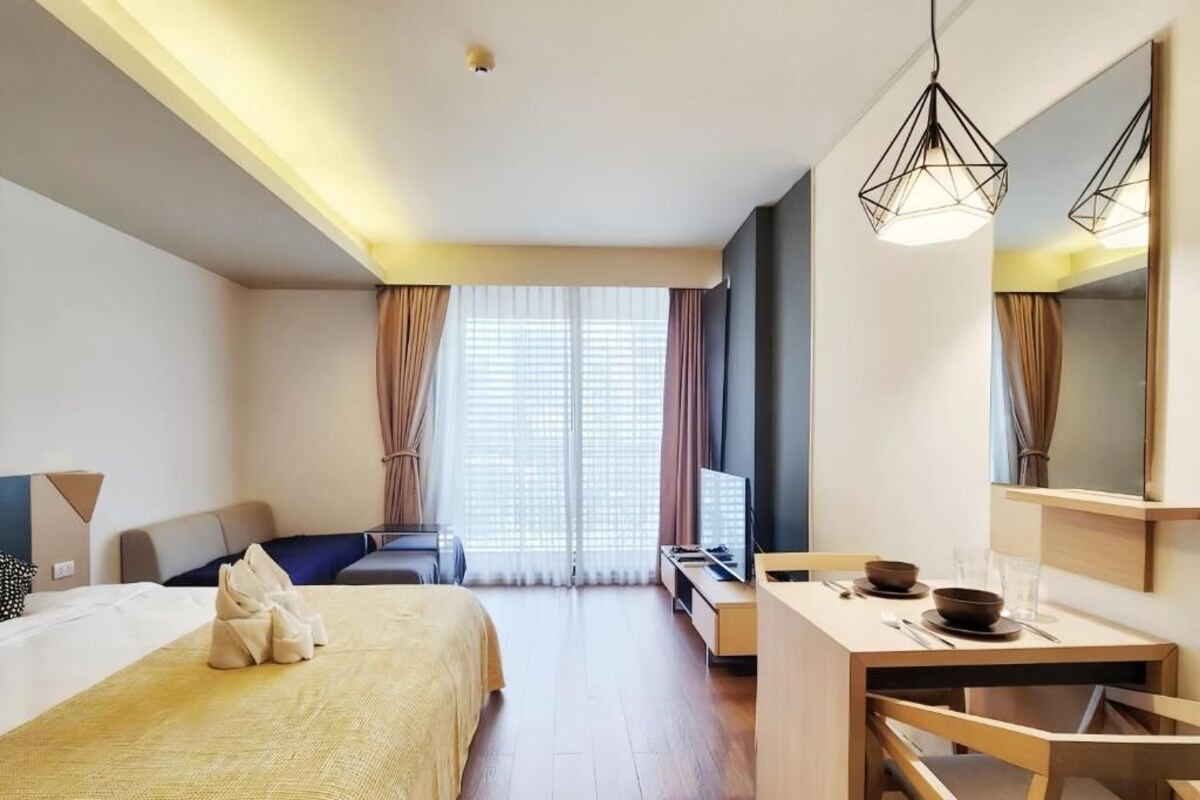 A hotel room with a bed, a desk, a chair, a television, and a large window with curtains.