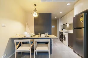 A compact kitchen with a built-in washing machine, a refrigerator, and a dining area with chairs and a table set for two.