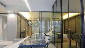 Una habitación de hotel moderna con separador de vidrio, una mesa de comedor con cubierta de mármol y una cama con cabecera blanca.