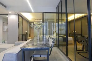 A modern hotel room with a glass partition, a marble-topped dining table, and a bed with a white headboard. - Circle S Sukhumvit 12 Bangkok (Krung Thep Maha Nakhon)