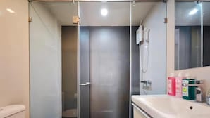 Baño con cabina de ducha de vidrio, inodoro y lavabo con artículos de aseo.