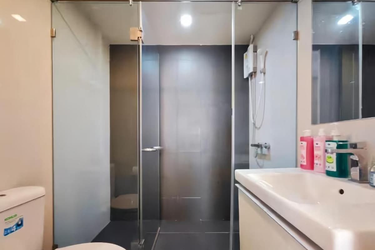 A bathroom with a glass shower enclosure, a toilet, and a sink with toiletries.