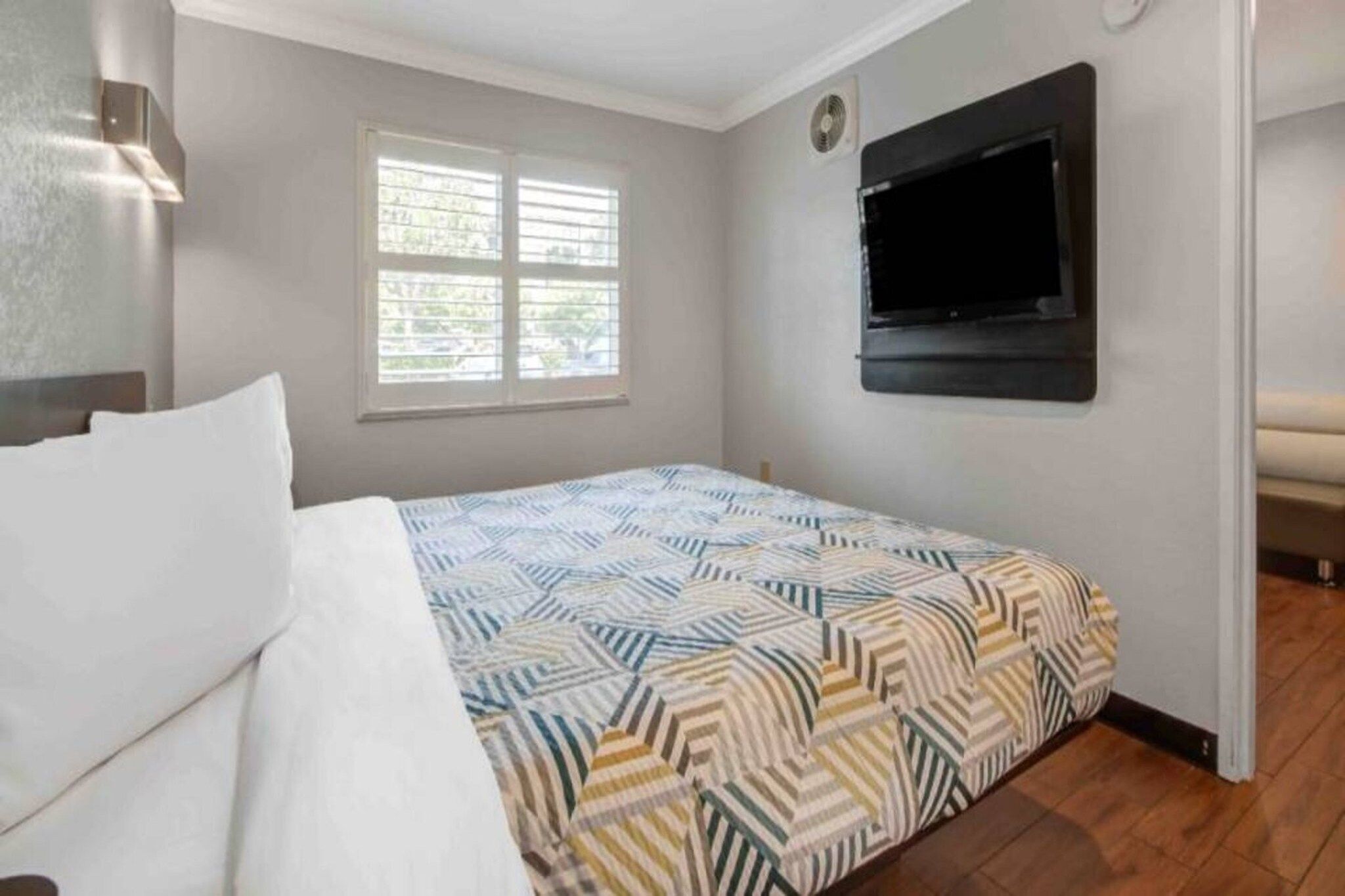 A bedroom with a bed, a window, a wall-mounted TV, and a door.
