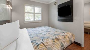 A bedroom with a bed, a window, a wall-mounted TV, and a door.