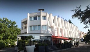 Un hotel de diseño moderno, con una entrada de vidrio curvo y un toldo rojo.