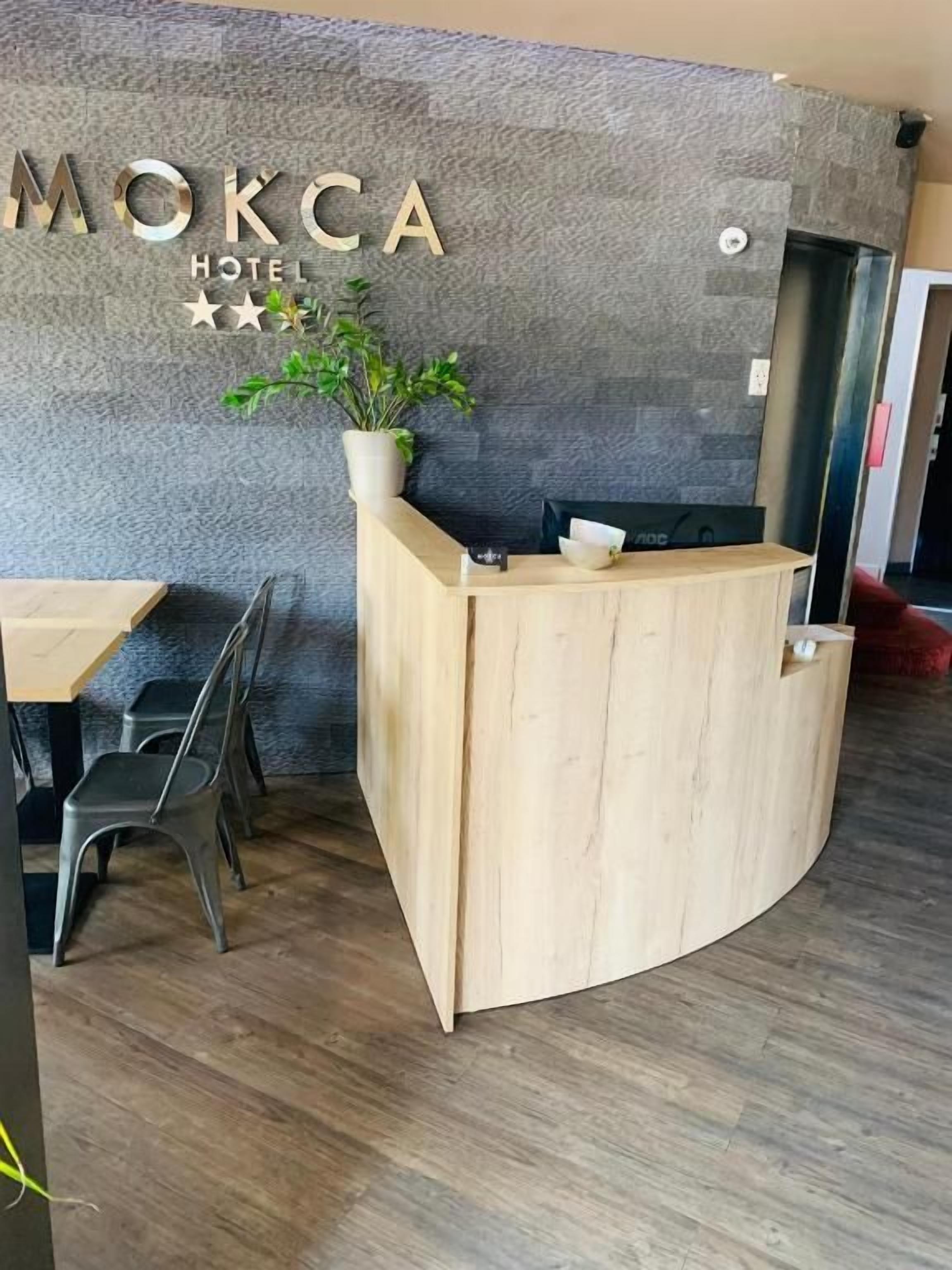 Una recepción con detalles de madera, una planta en maceta y un cartel que dice 'MOKCA HOTEL'.