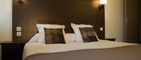Une chambre d’hôtel avec un grand lit, deux tables de chevet et des lampes fixées au mur.