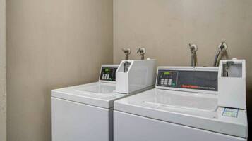 Fileira de máquinas de lavar roupa brancas com mostradores digitais, provavelmente em um hotel ou estabelecimento similar.