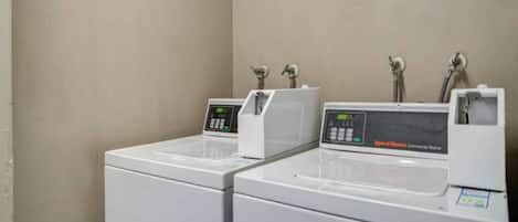 Een rij witte wasmachines met digitale displays, waarschijnlijk in een hotel of vergelijkbare accommodatie.
