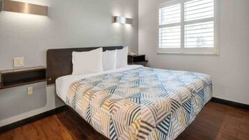 A hotel room with a bed, a nightstand, a wall-mounted light, and a window with blinds.