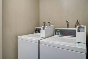 A row of white laundry machines with digital displays, likely in a hotel or similar accommodation.