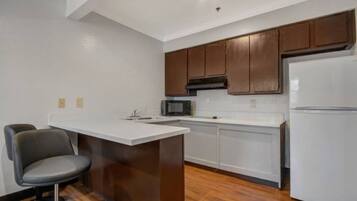 A kitchen with a white countertop, a microwave, a refrigerator, and wooden cabinets.