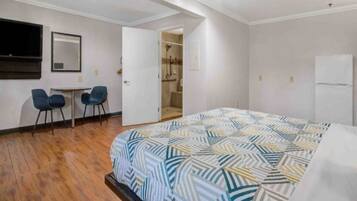 Una habitación de hotel con cama, escritorio, dos sillas, espejo y armario.