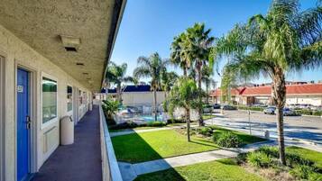 A hotel corridor with a blue door, a covered outdoor area with palm trees, and a parking lot in the background.