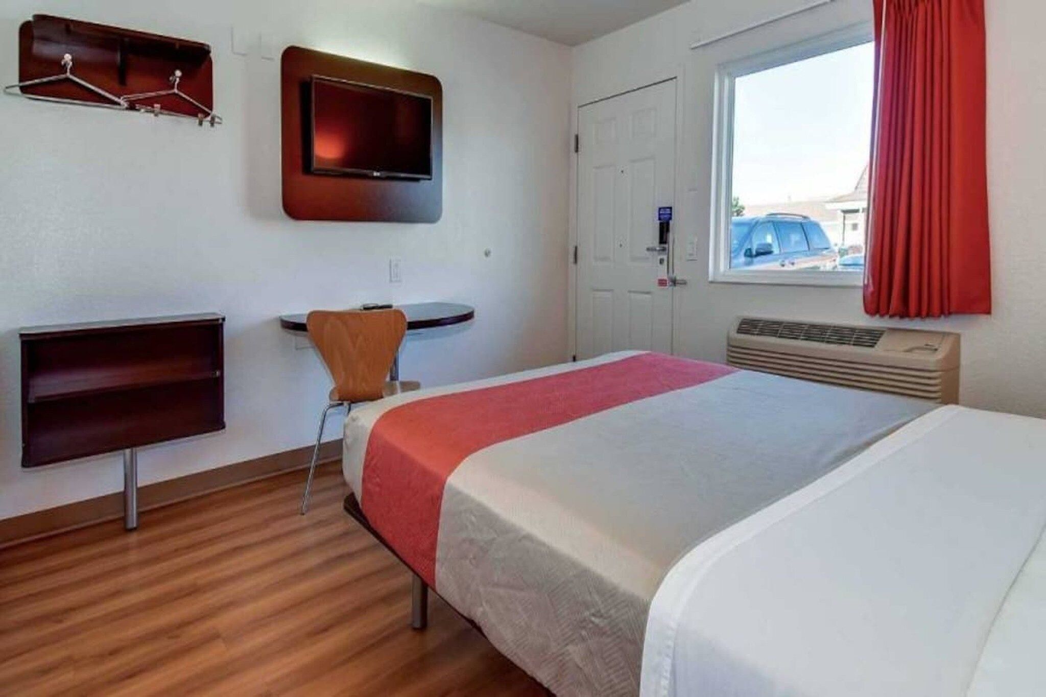 Una habitación de hotel con cama, escritorio, silla, televisión y ventana con cortinas.