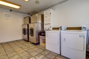 A laundry room with two washing machines, a dryer, and a sign indicating soap and bleach.