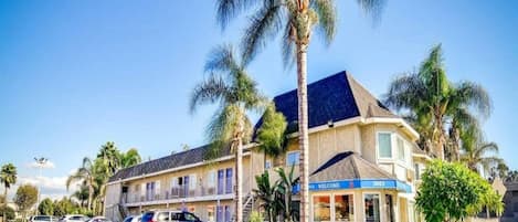 Un motel composé d’un bâtiment à deux étages, d’une enseigne « Bienvenue » et d’un parking où sont stationnées plusieurs voitures.
