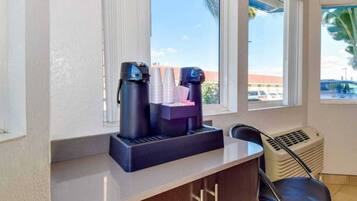 A room with a window, a coffee machine, and a chair.