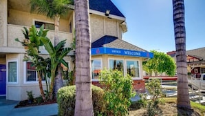 A hotel with a 'Welcome' sign, palm trees, and a clear blue sky. - 2 Full Beds | Smoking (Riverside)