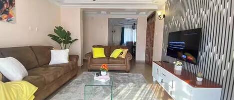 A living room with a sofa, a coffee table, a TV, and a decorative wall.