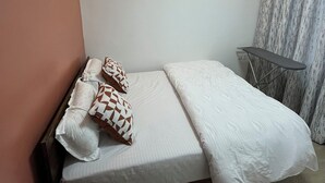 A bedroom with a bed, pillows, a small table, and a chair. - JKIA Terminal Luxore  (Syokimau)