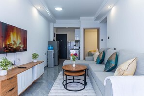 A modern living room with a sofa, a coffee table, a TV, and a kitchen area in the background. - JKIA Terminal Luxore  (Syokimau)