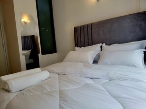 A neatly made bed with white linens and pillows, a dark headboard, and a wall-mounted light fixture. - JKIA Terminal Luxore  (Syokimau)