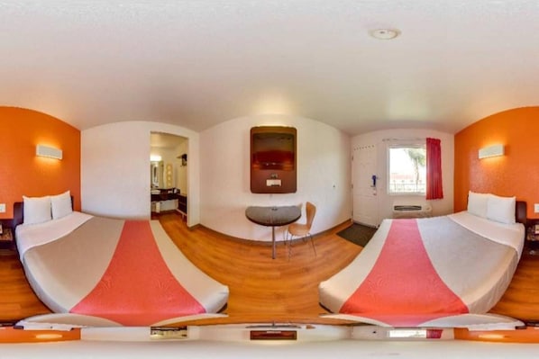 A room with two beds, a small table, and a mirror on the wall.