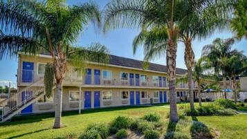 A hotel with a two-story structure, multiple rooms with blue doors, a central staircase, and a well-maintained lawn with palm trees.