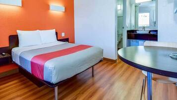 Una habitación de hotel con cama, una mesa redonda y un baño visible a través de una puerta abierta.