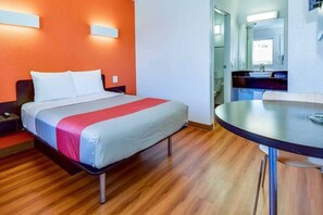 Una habitación de hotel con cama, una mesa redonda y un baño visible a través de una puerta abierta.